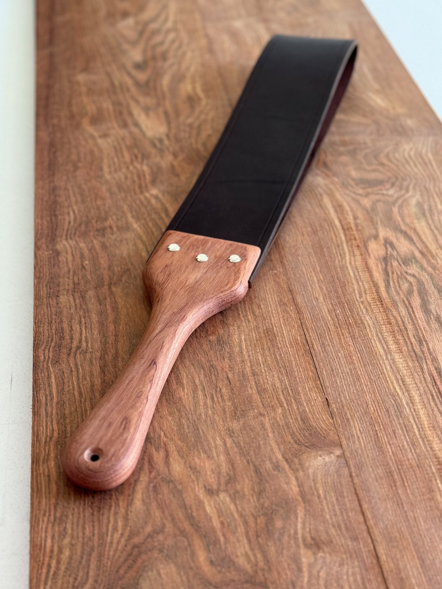 Chocolate brown leather spanking strap looped and affixed to a Bubinga hardwood handle with Chicago screws